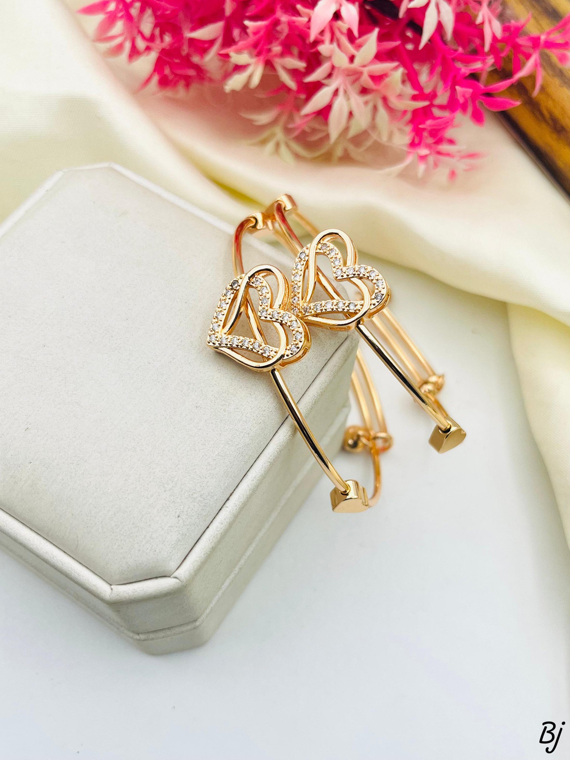 Gold heart-shaped earrings on a white box with pink flowers in the background