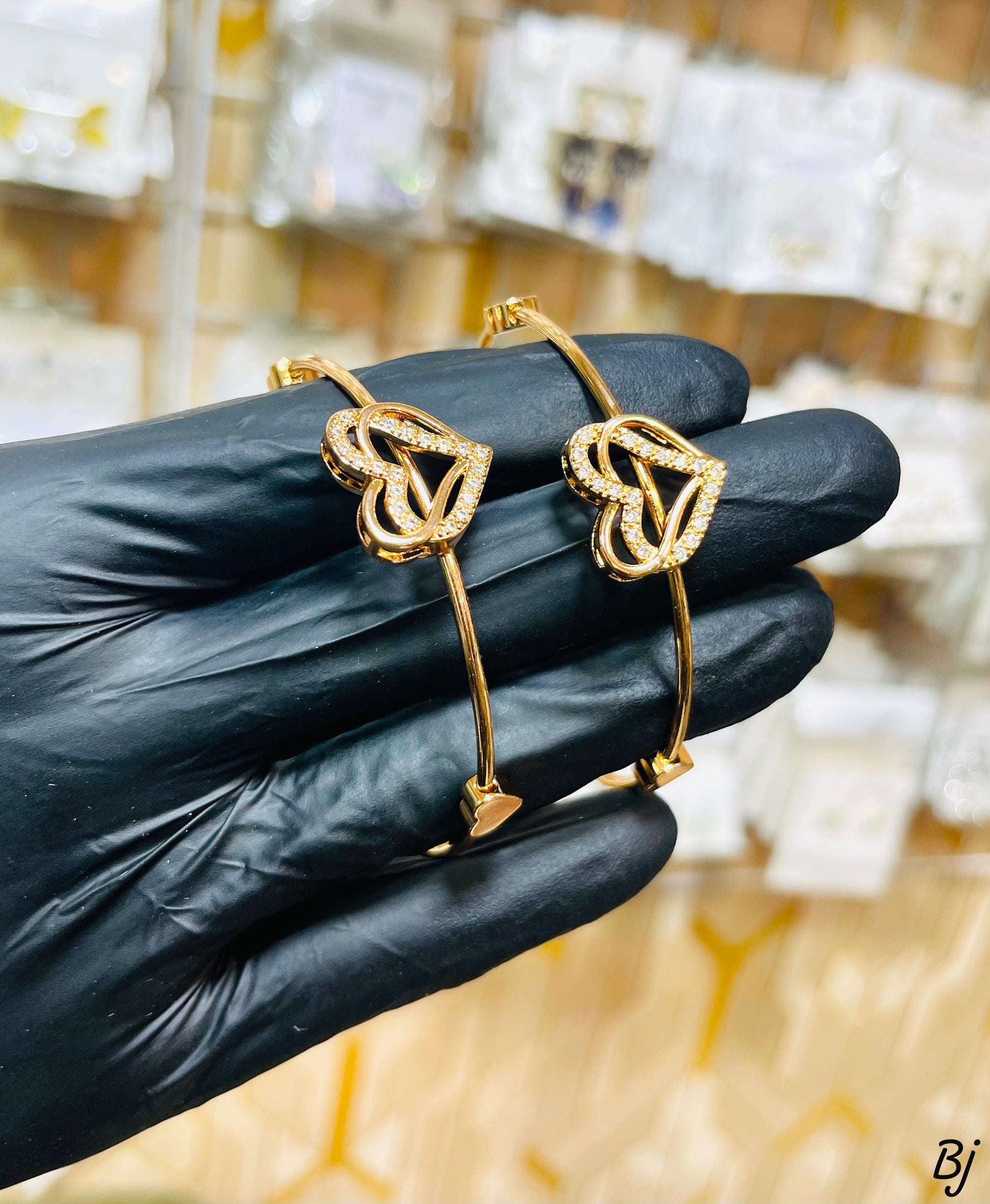 Gold bracelet with heart design held by a gloved hand against a blurred background