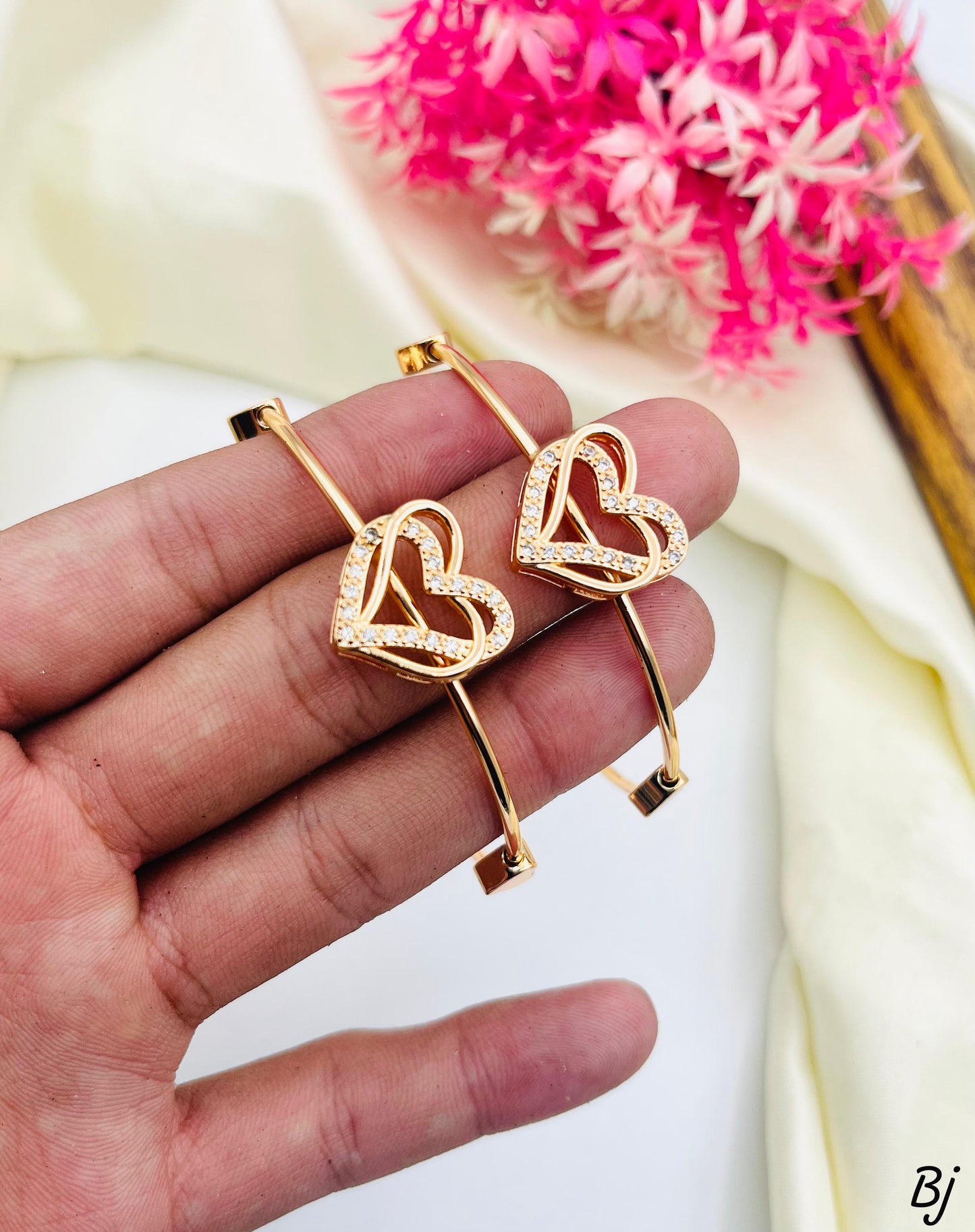Gold heart-shaped earrings held in a hand with pink flowers in the background