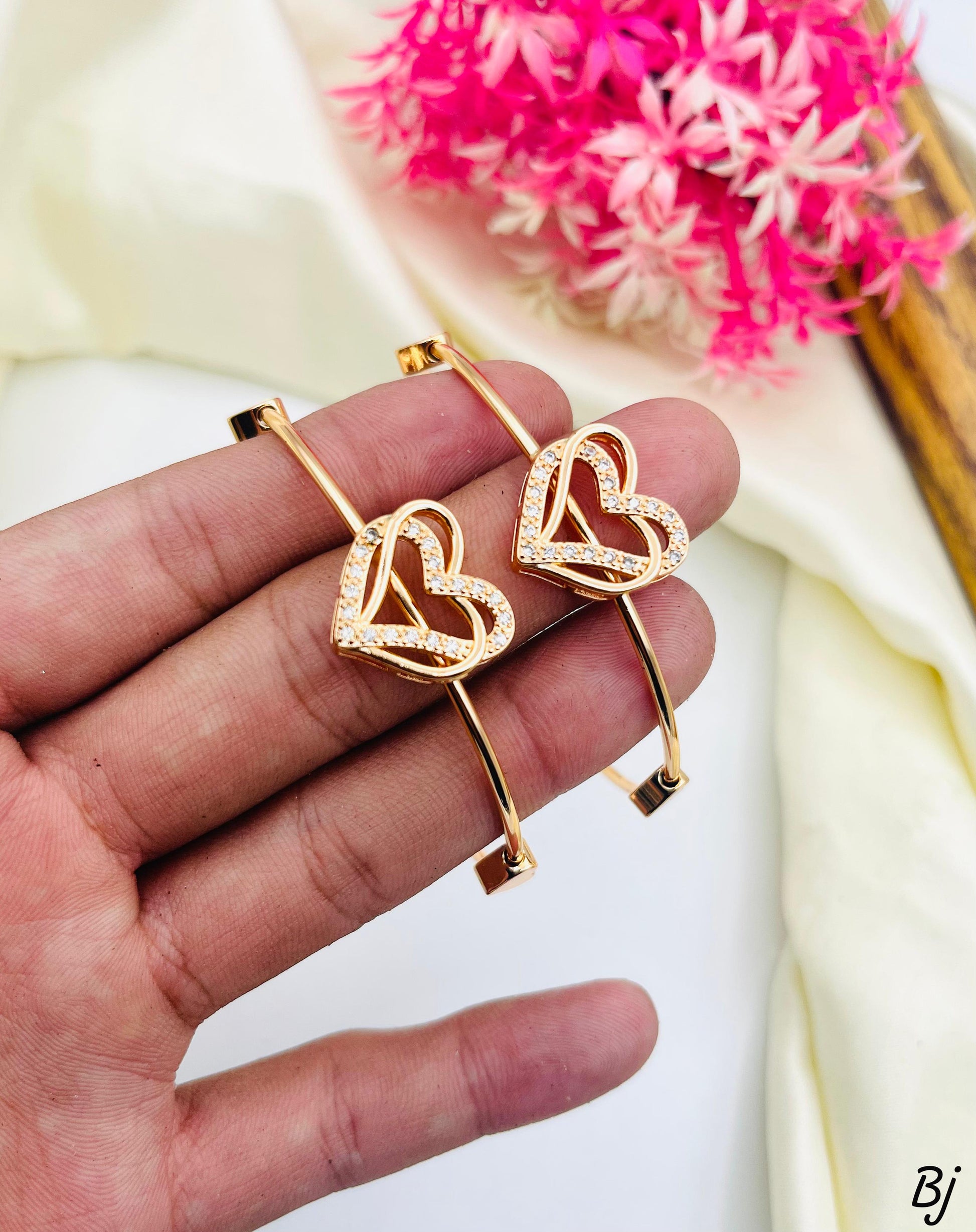 Gold heart-shaped earrings held in a hand with pink flowers in the background